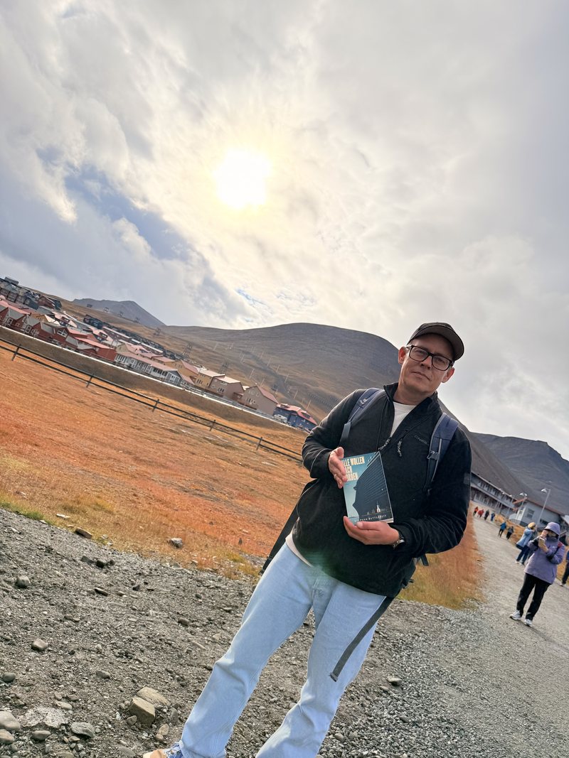 Stephan Buttgereit mit dem Roman Alle wollen nach Norden in Longyearbyen auf Spitzbergen, dahinter herbstlich gefärbte Tundra und die Berge über der Stadt